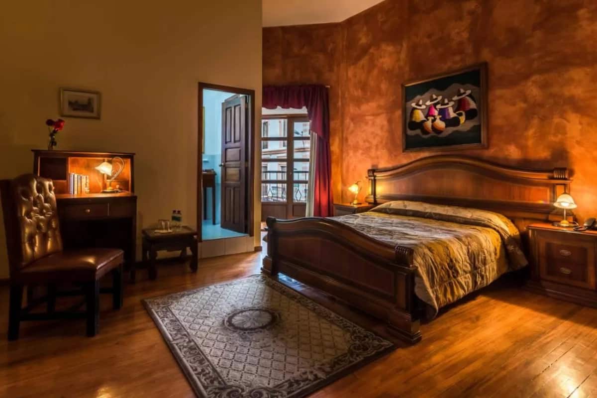 Une chambre d’hôtel avec un grand lit, un bureau avec une lampe, une chaise et une vue sur l’extérieur par une porte.