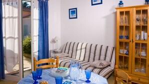 A room with a striped sofa, a wooden cabinet with glass doors, and a dining table with blue glassware. - Madame Vacances Les Mas de St Hilaire (Saint-Hilaire-de-Riez)