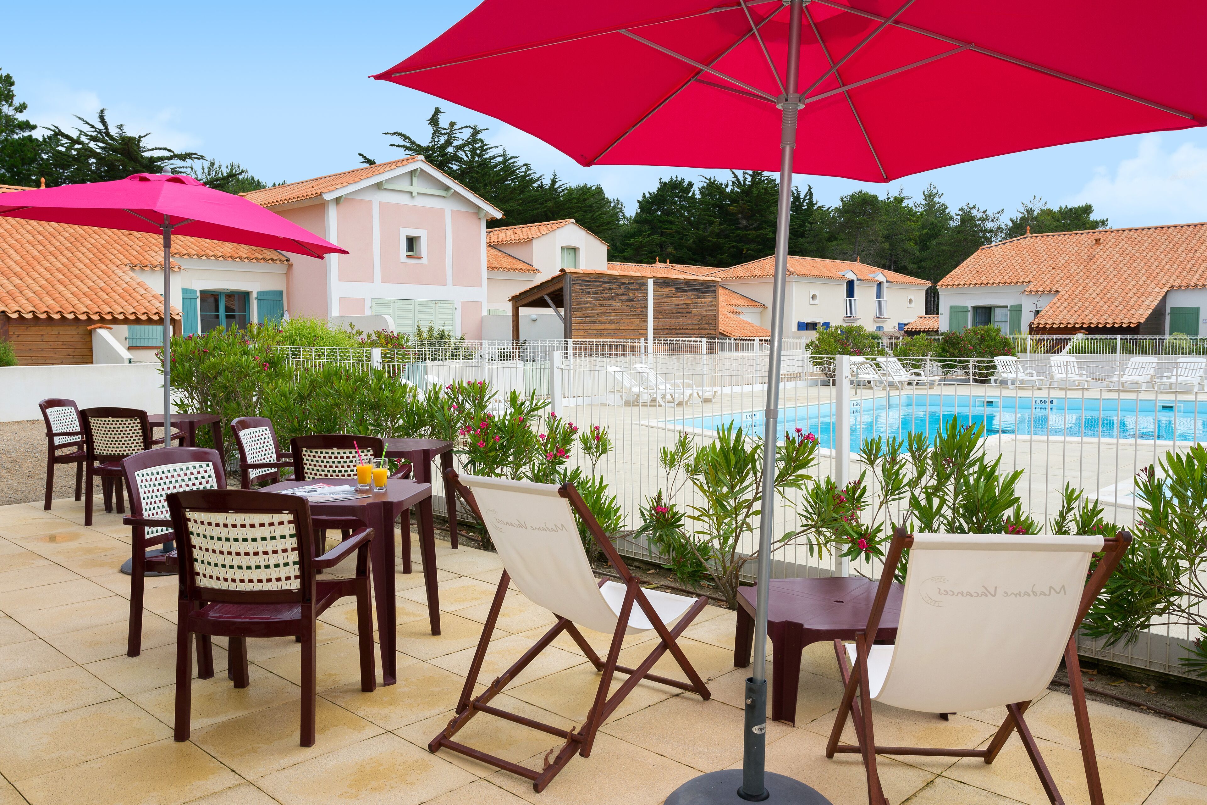 Un espace aménagé au bord de la piscine, avec des chaises longues, un parasol rouge et une piscine.