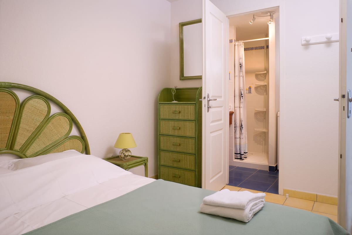 A bedroom with a bed, a green dresser, a nightstand with a lamp, and an open door leading to a bathroom.