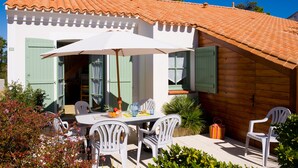 A white building with green shutters, a tiled roof, and a patio with white chairs and a table. - Madame Vacances Les Mas de St Hilaire (Saint-Hilaire-de-Riez)
