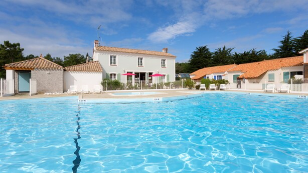 A swimming pool with clear blue water, surrounded by white buildings with red-tiled roofs. - Madame Vacances Les Mas de St Hilaire (Saint-Hilaire-de-Riez)
