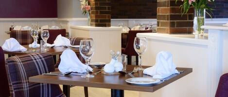 A restaurant setting with a brick wall, plaid chairs, and a vase of flowers on the counter.