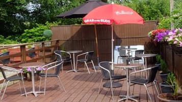 An outdoor patio with metal chairs and tables, a red umbrella with 'Grab Some Buds' text, and a wooden fence in the background.
