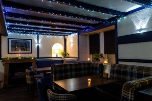 A cozy restaurant with plaid booths, a fireplace, and string lights. - The Crown Hotel (Newton Stewart)