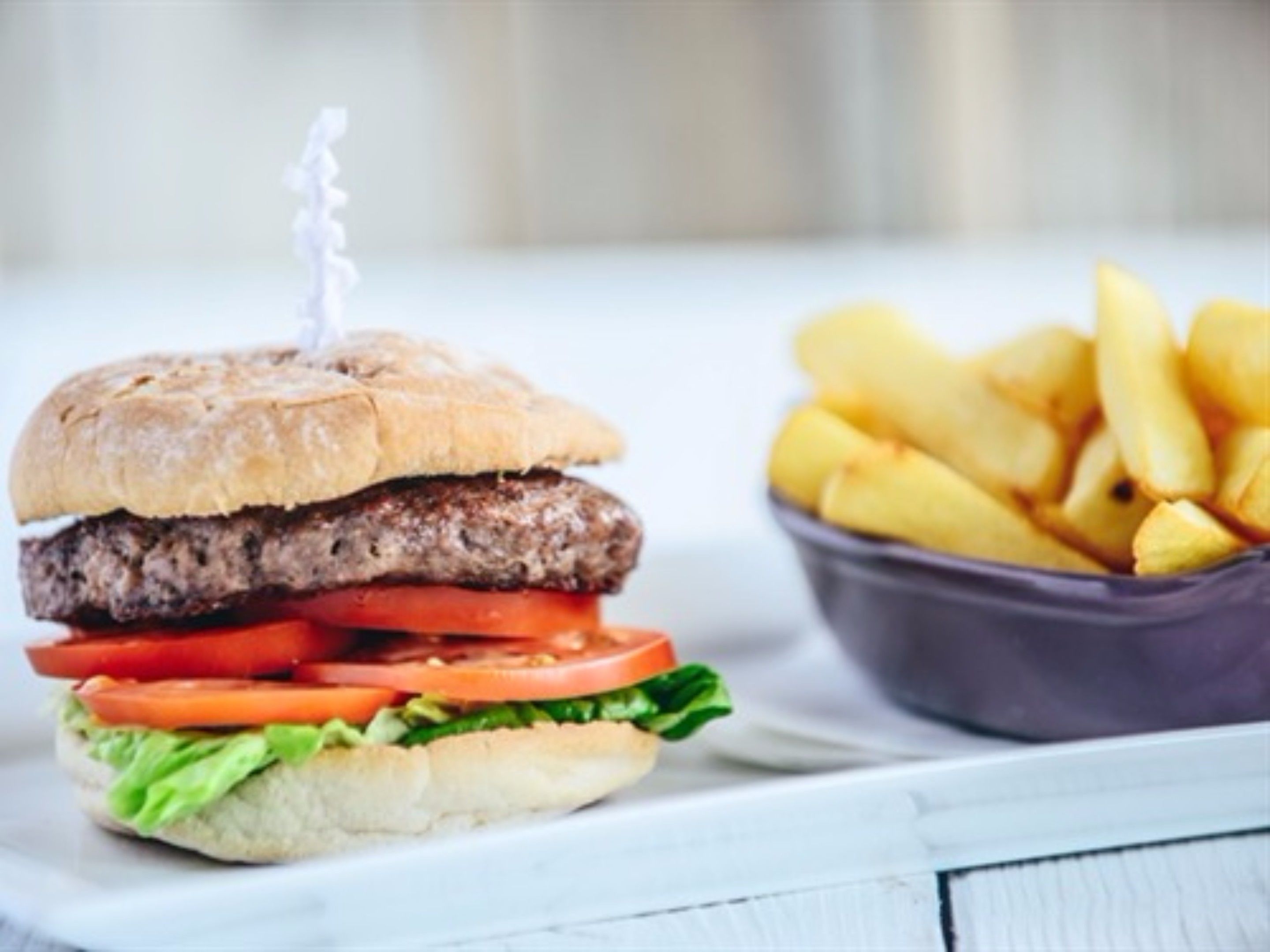 A hamburger with a toothpick in the bun, accompanied by a bowl of fries.