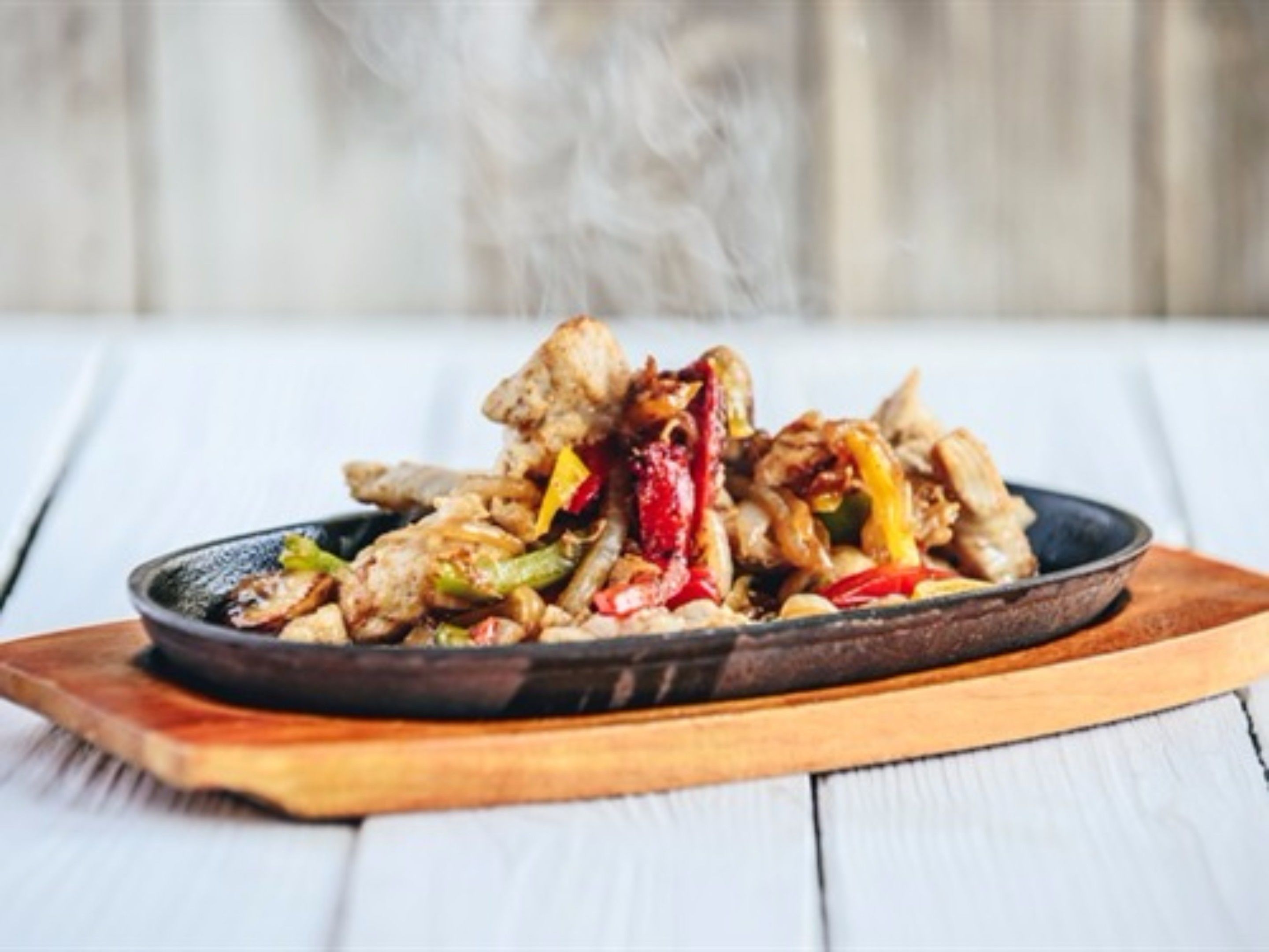 A stir-fried dish with vegetables and meat on a black plate on a wooden board.