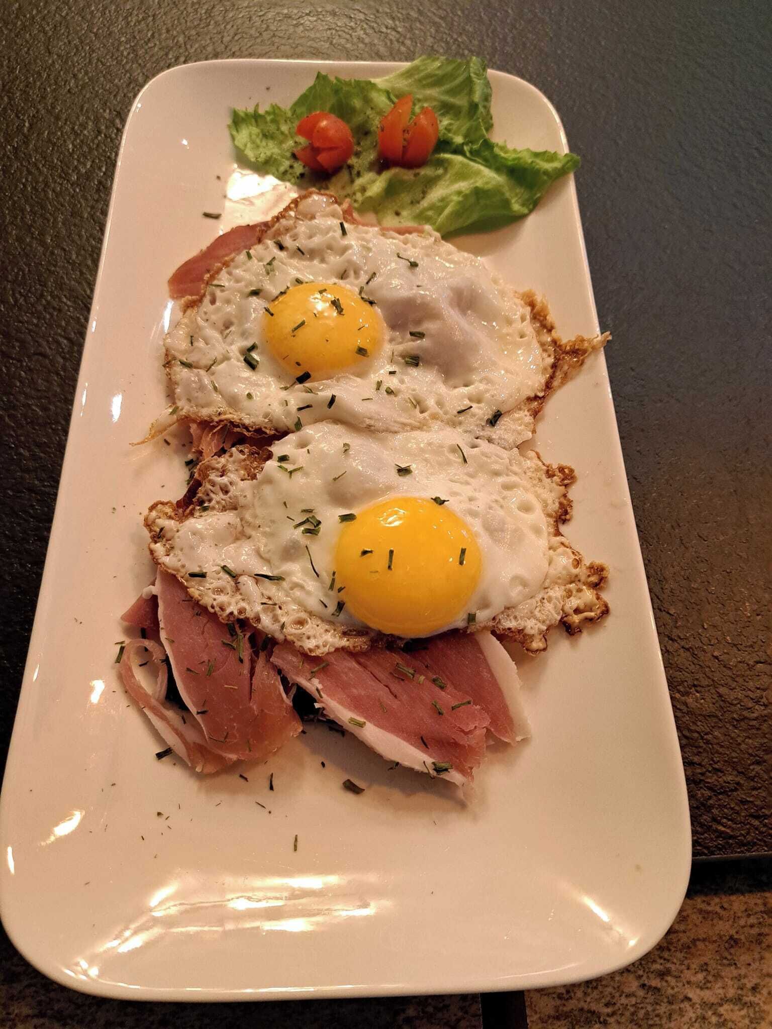 Une assiette avec deux œufs au plat, du jambon et une salade en accompagnement.