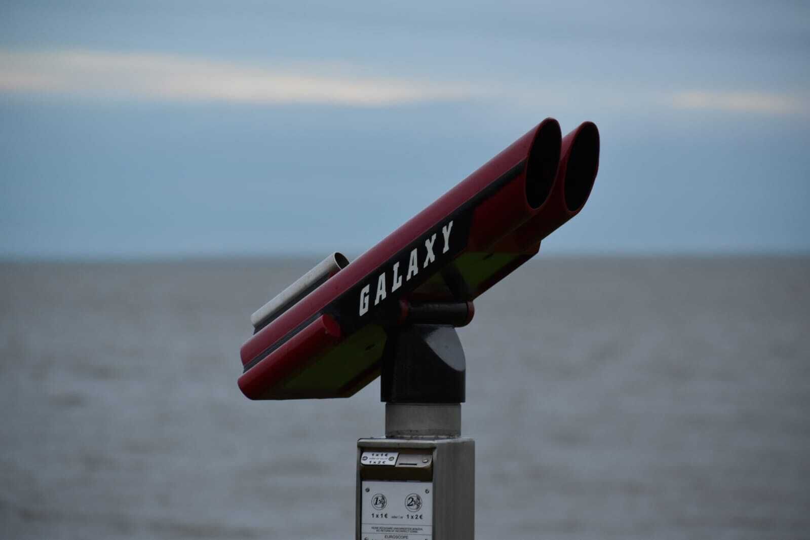 Un telescopio con la etiqueta 'GALAXY' montado en una estructura, con vista al mar.