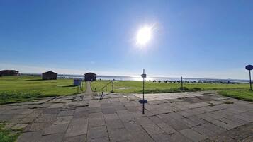 A paved pathway leading to a grassy area with a view of the sea and buildings in the distance.