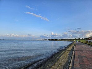 A waterfront promenade with a brick walkway, calm water, and distant wind turbines. - Hotel Arche Noah (Wangerland)