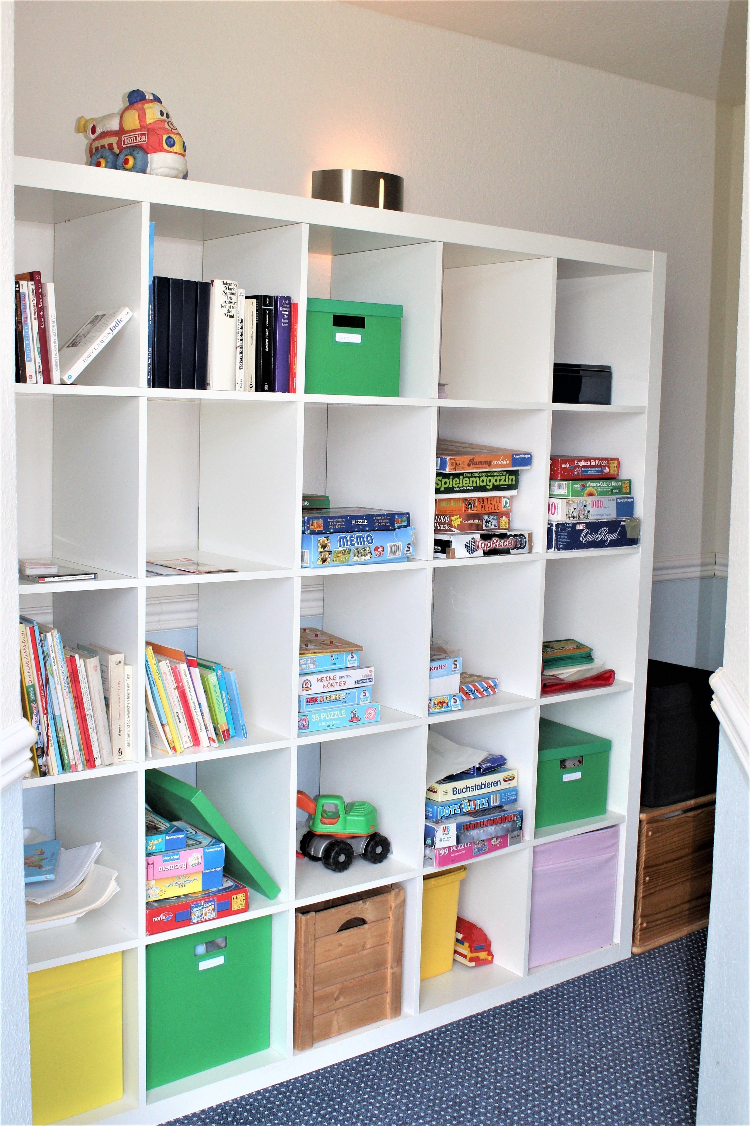 Een witte boekenkast met diverse spullen, zoals boeken, puzzels en speelgoed.