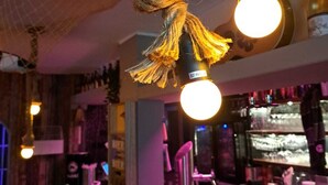 A bar area with hanging lights, a bar counter, and shelves with bottles. - Hotel Arche Noah (Wangerland)