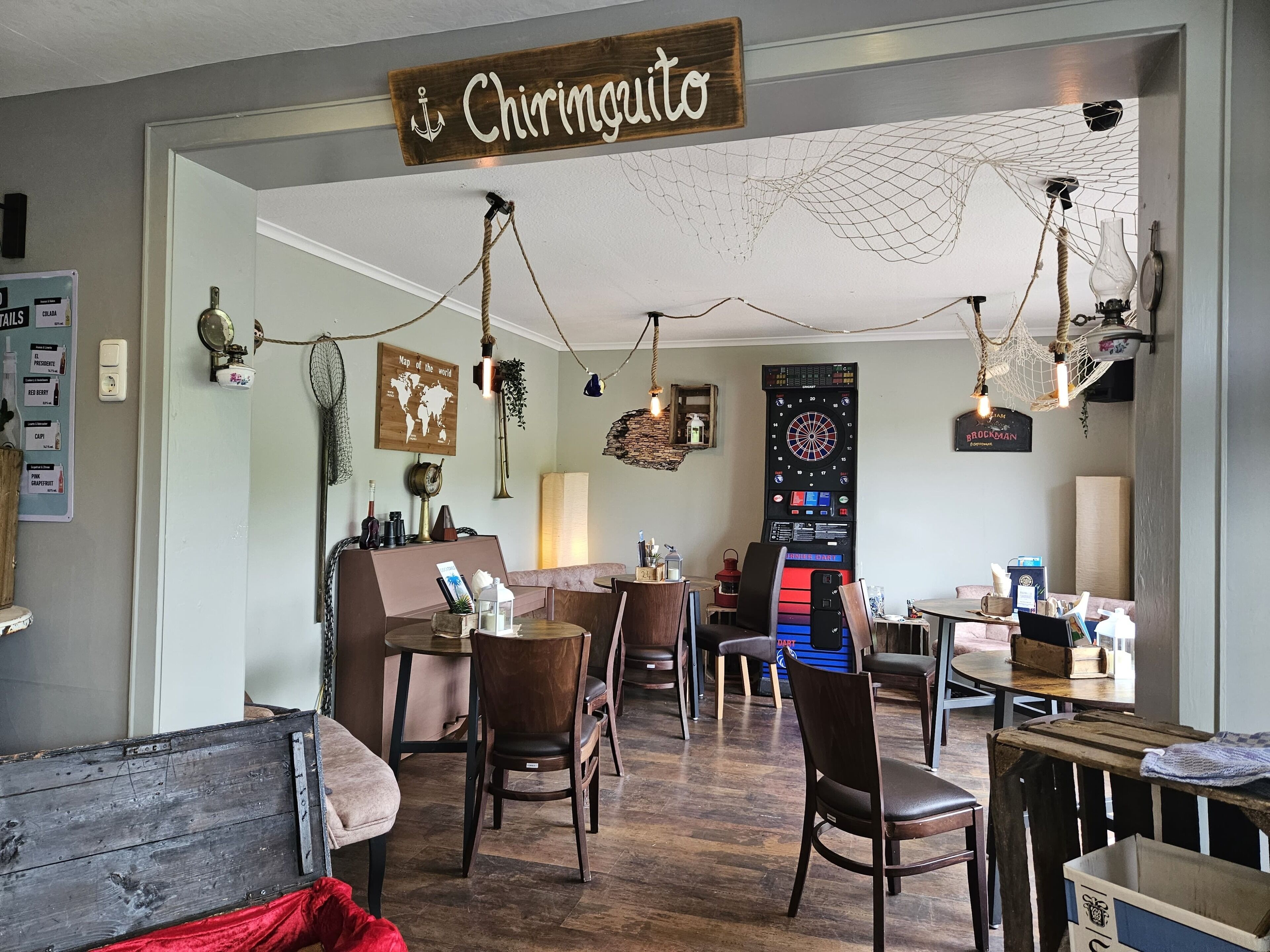 Een gezellig, nautisch ingericht interieur met een dartbord, houten meubels en een bordje met de tekst 'Chiringuito'.