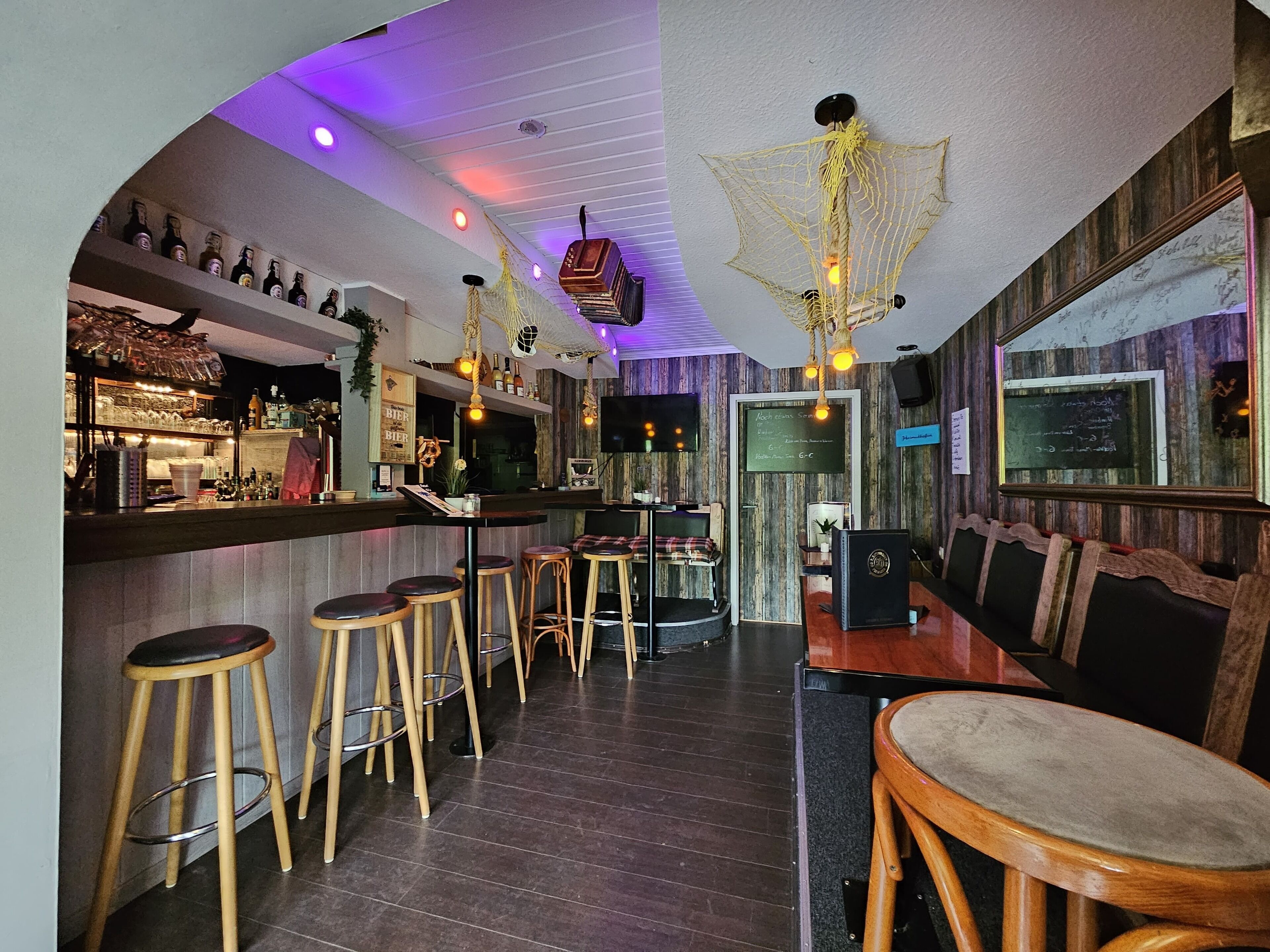 A bar area with wooden stools, a counter with bottles, and a neon light fixture.