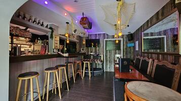 A bar area with wooden stools, a counter with bottles, and a neon light fixture.