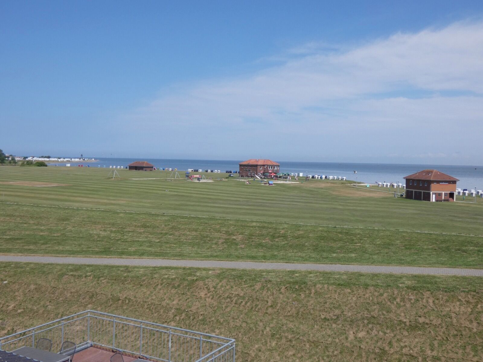 A large, open grassy field with a few buildings and a clear view of the sea in the background.