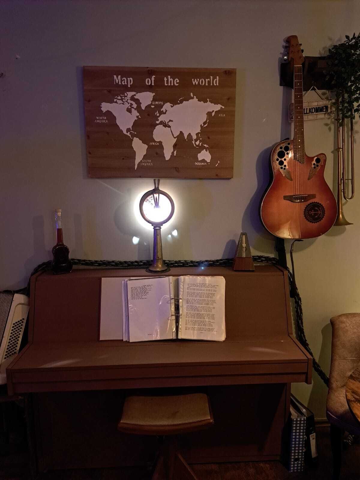 Una habitación con un escritorio de madera, un mapa-globo, una guitarra y una lámpara.
