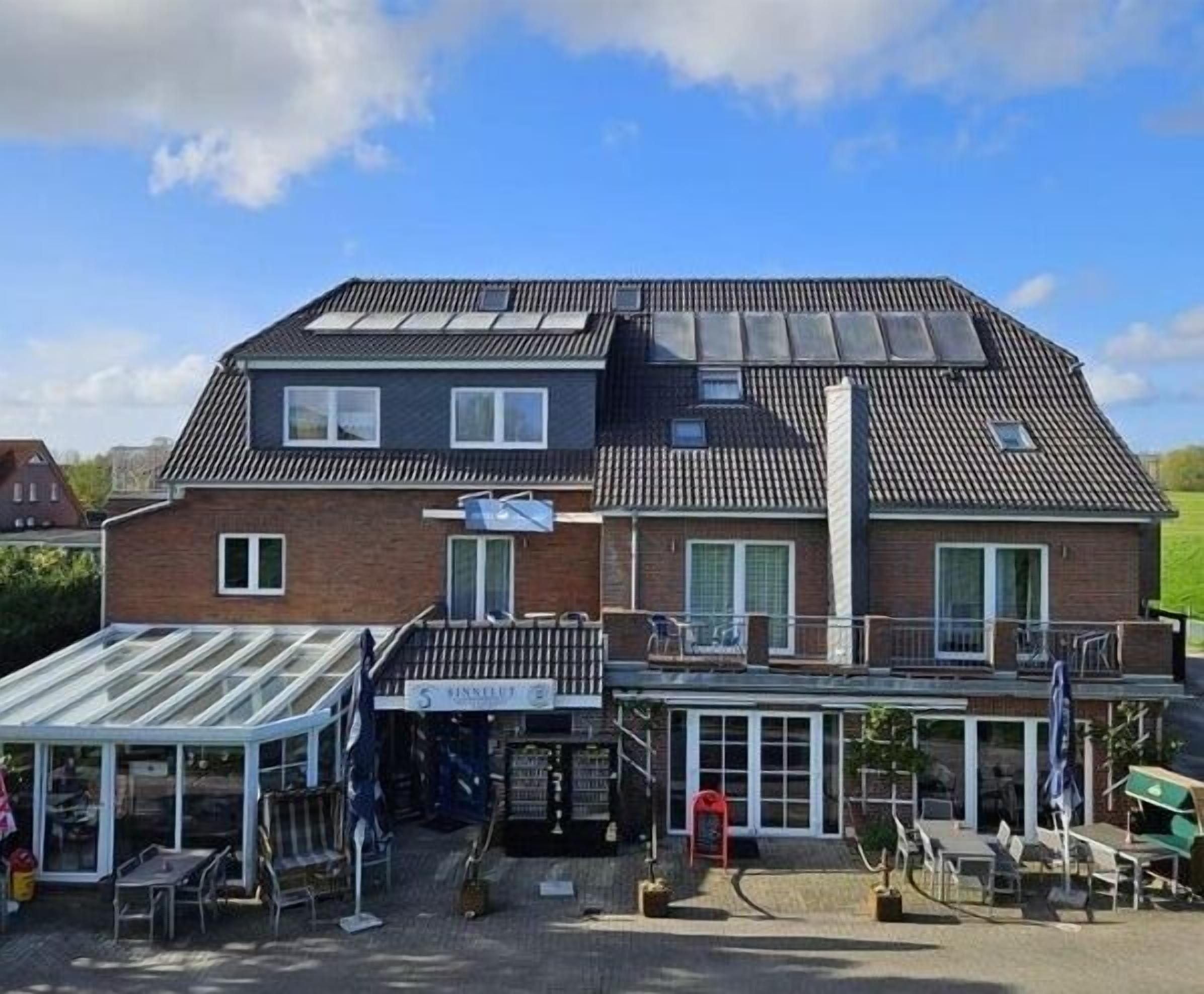 Un bâtiment à deux étages, doté d’un toit plat, d’un espace extérieur couvert aménagé en coin salon et d’une enseigne indiquant qu’il s’agit d’un commerce ou d’un prestataire de services.