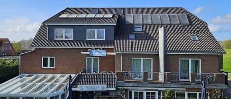 Un bâtiment à deux étages, doté d’un toit plat, d’un espace extérieur couvert aménagé en coin salon et d’une enseigne indiquant qu’il s’agit d’un commerce ou d’un prestataire de services.