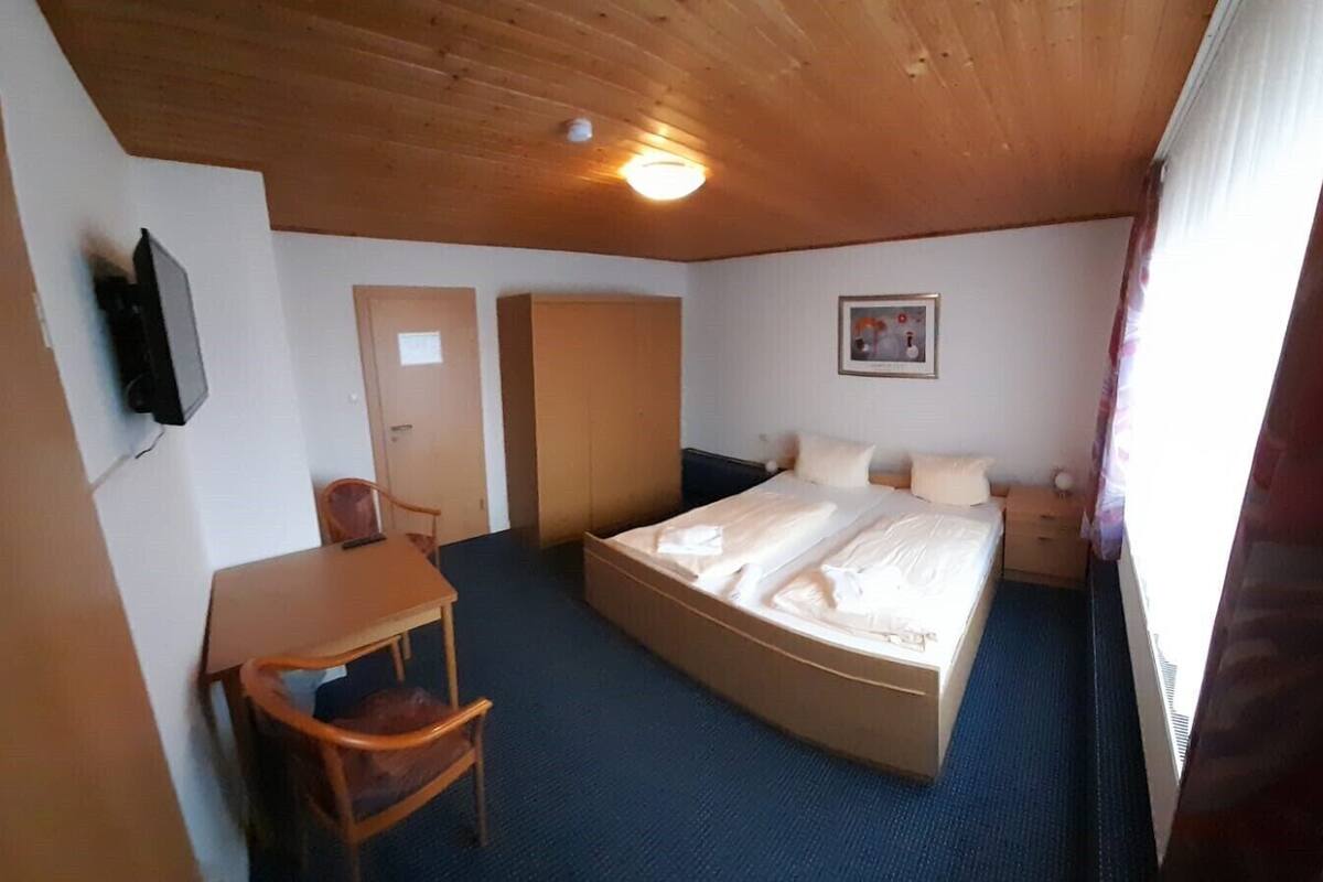 A room with a bed, a desk, a chair, a wardrobe, a television, and a picture on the wall.