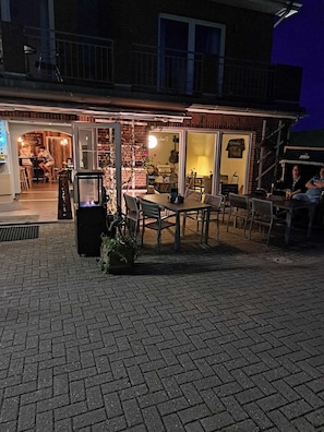 An outdoor seating area with brick flooring, tables, and chairs. - Hotel Arche Noah (Wangerland)