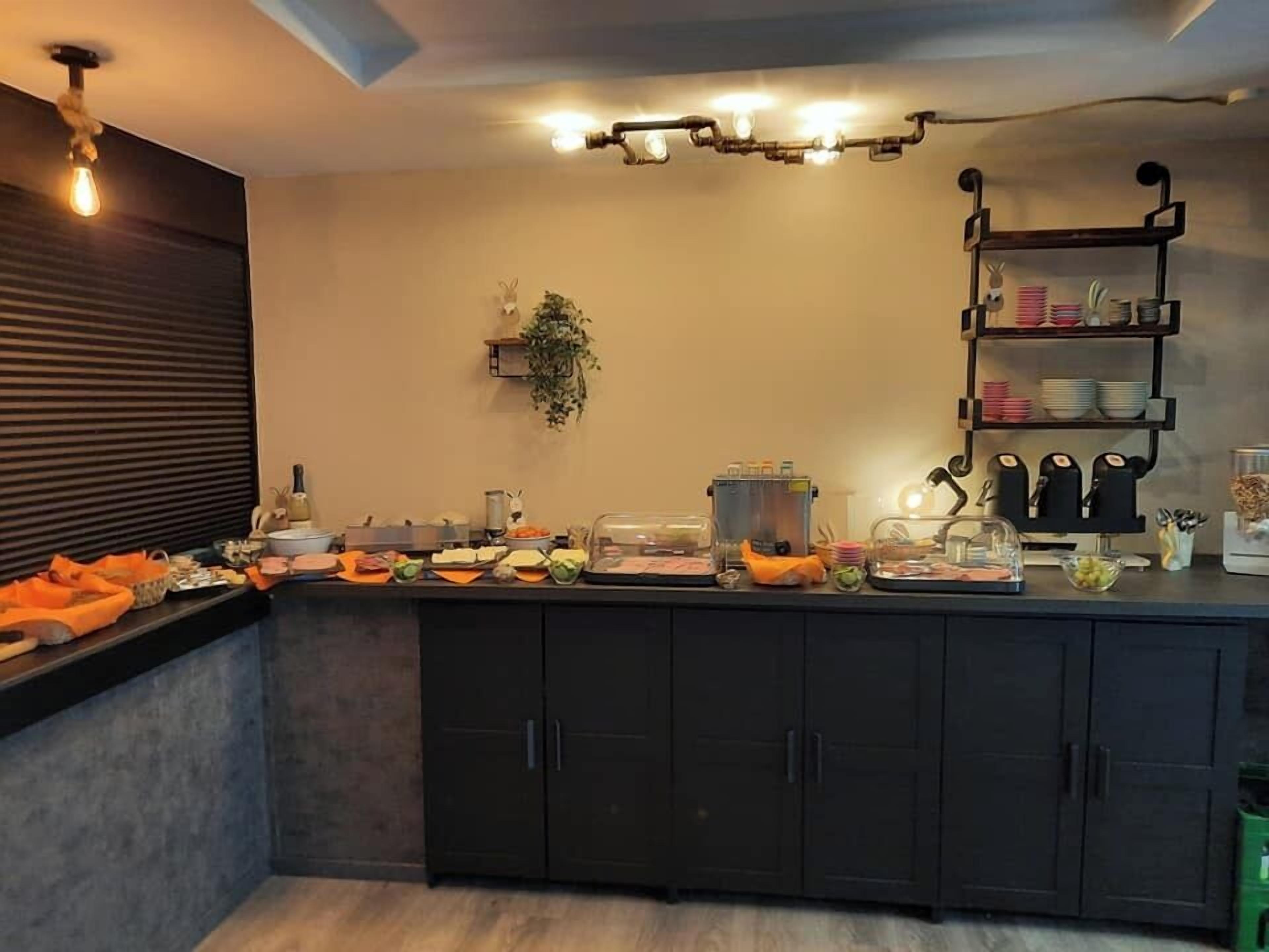 Una cocina con mesas tipo bufé, que incluyen una estación de café, un frutero y diversos alimentos en la encimera.