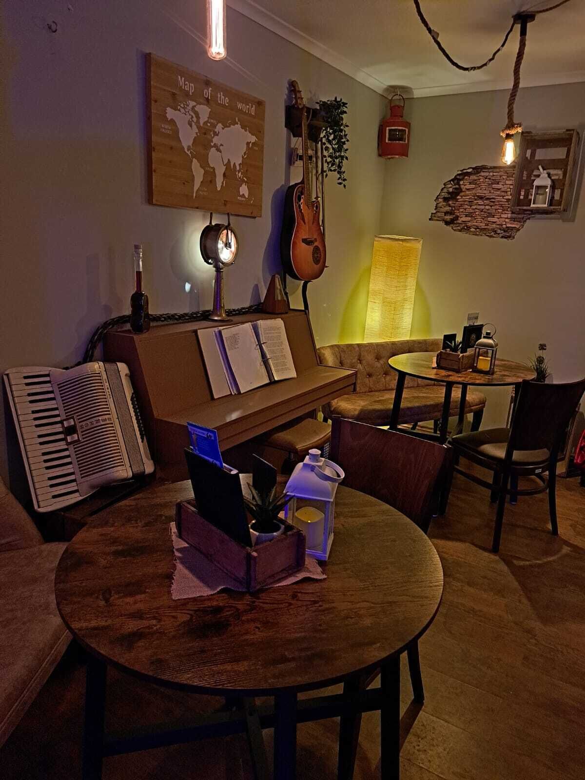 A cozy living room with a piano, a guitar, and a vintage radio. There is a round table with chairs and a small lamp.