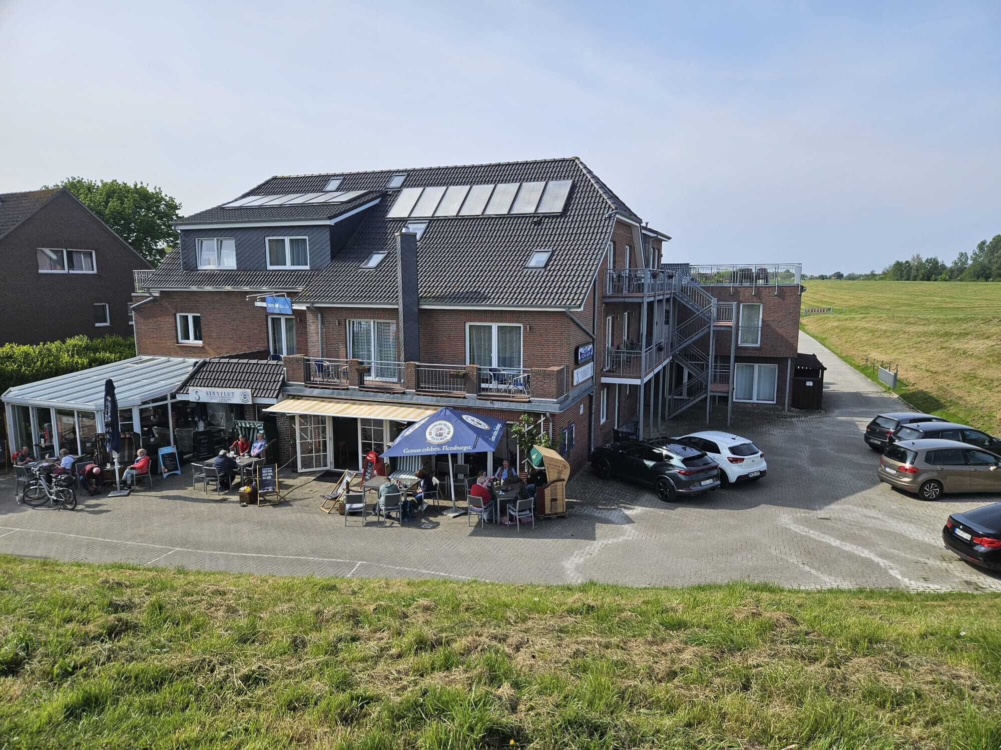 A two-story building with a covered outdoor seating area, a staircase, and parked cars.