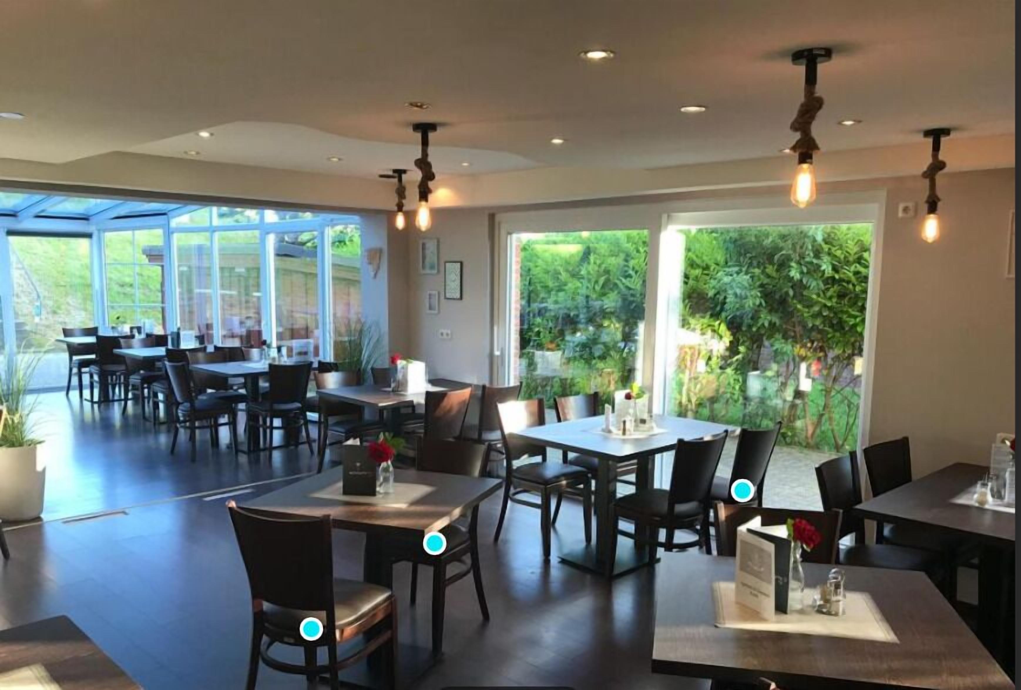 Un espace repas moderne, doté de tables et de chaises, de grandes fenêtres et de luminaires suspendus.