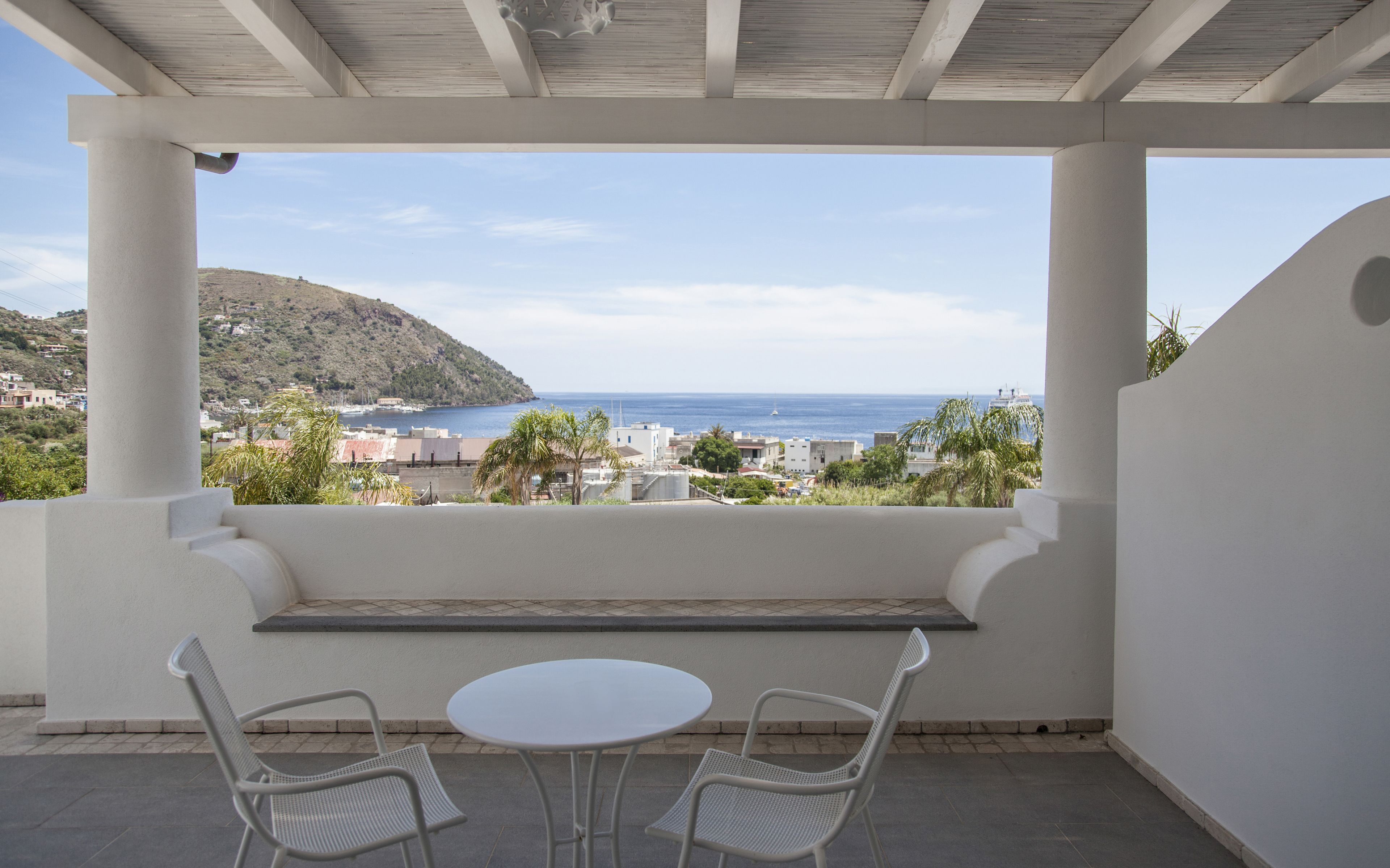 A covered outdoor seating area with a view of the sea and a hillside.