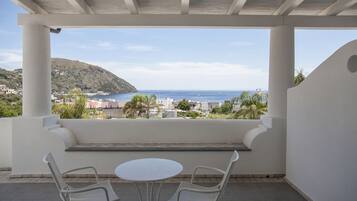 A covered outdoor seating area with a view of the sea and a hillside.