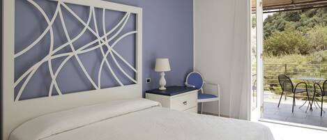 Un dormitorio con una cama grande, una mesita de noche con lámpara, una silla y vistas a un patio exterior con mesa y sillas.
