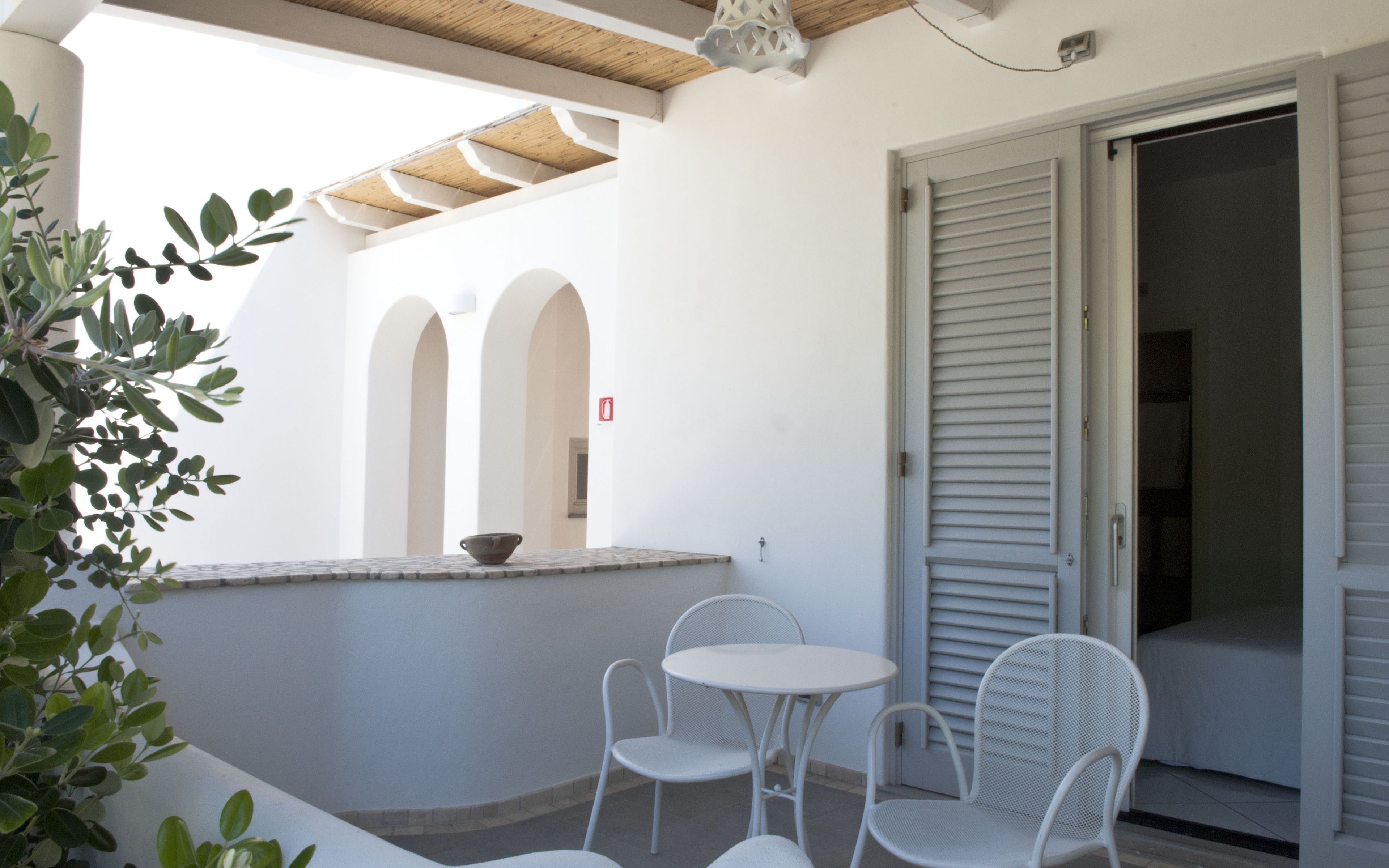 A balcony with white chairs, a small table, and a view of a building with arched doorways.