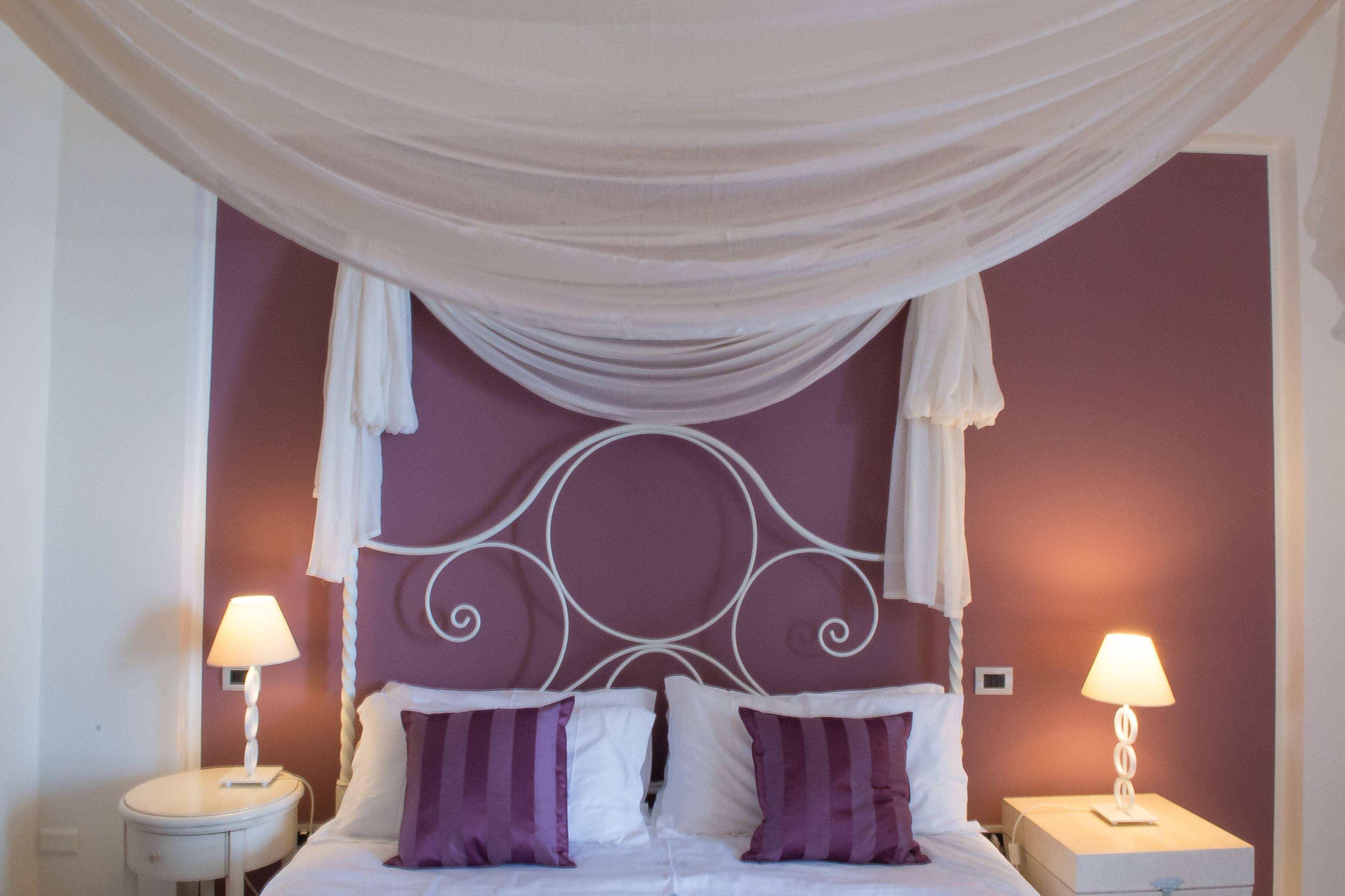 Een slaapkamer met een hemelbed, twee nachtkastjes met lampen en een hoofdeinde met decoratief design.