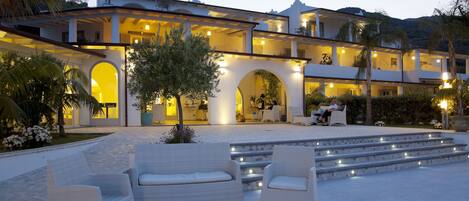 A large, multi-story building with a courtyard, outdoor seating, and illuminated steps.