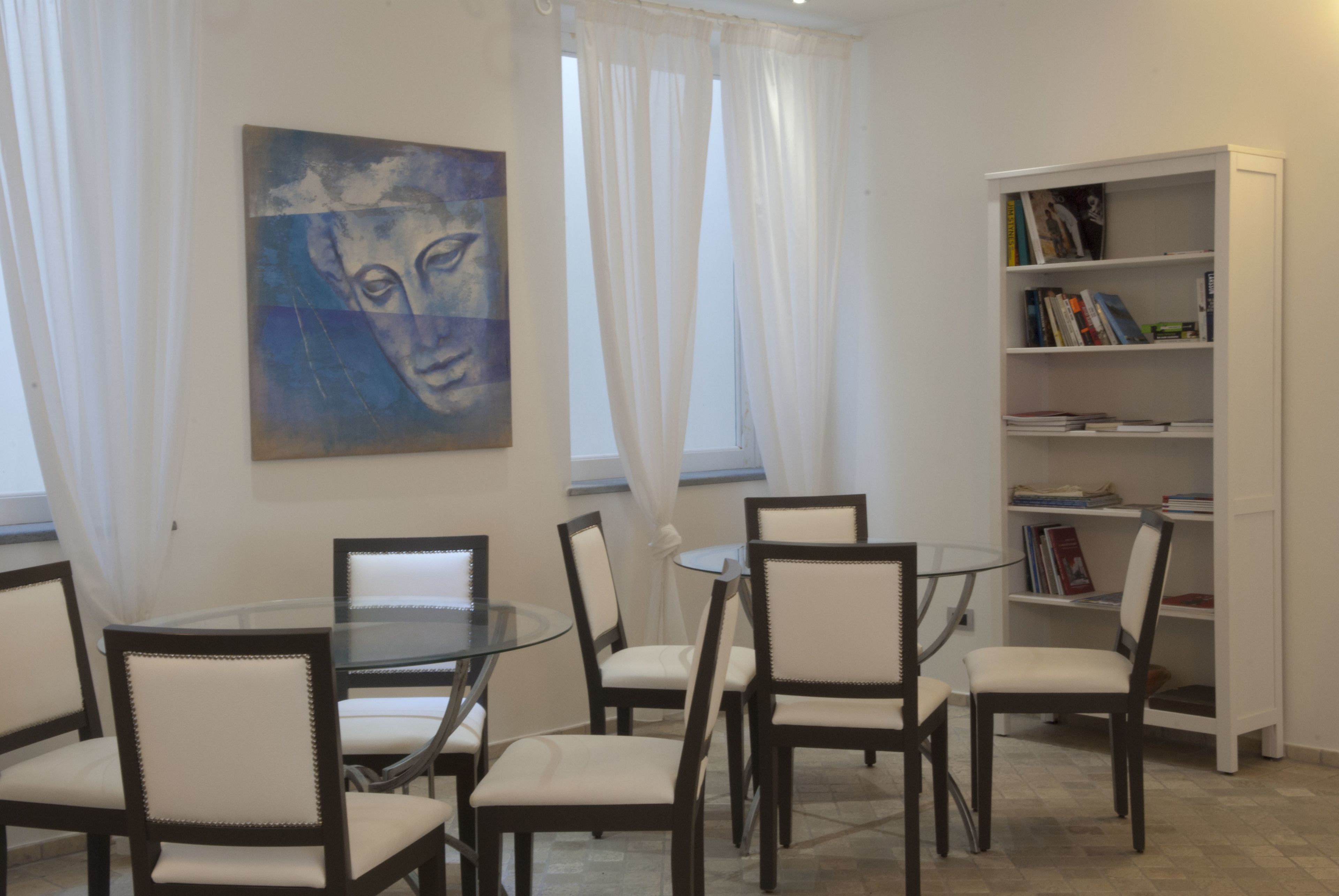Un coin repas avec une table ronde en verre entourée de chaises, une bibliothèque remplie de livres et un tableau accroché au mur.
