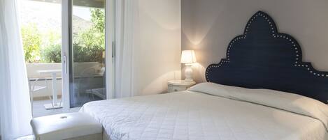 A bedroom with a bed, a nightstand, a lamp, and a view of an outdoor area with a table and chairs.