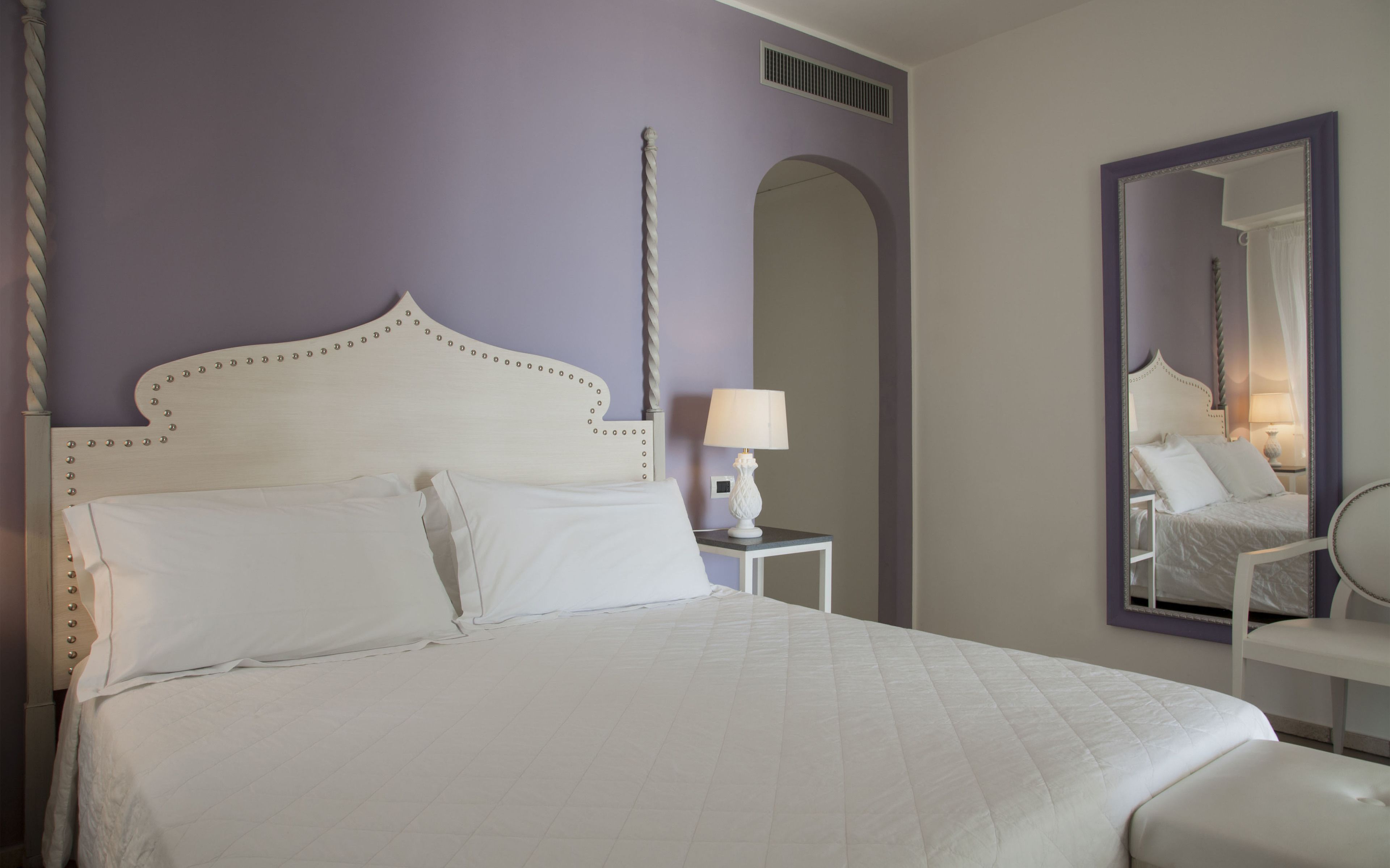 A neatly made bed with white linens in a room with purple walls.