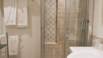 Une salle de bain avec une douche à parois de verre, un lavabo blanc et plusieurs serviettes blanches suspendues à un porte-serviettes.