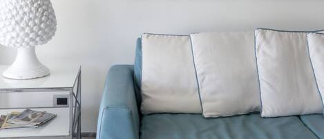 A modern living room with a blue sofa, white cushions, a white lamp, and two abstract paintings on the wall.