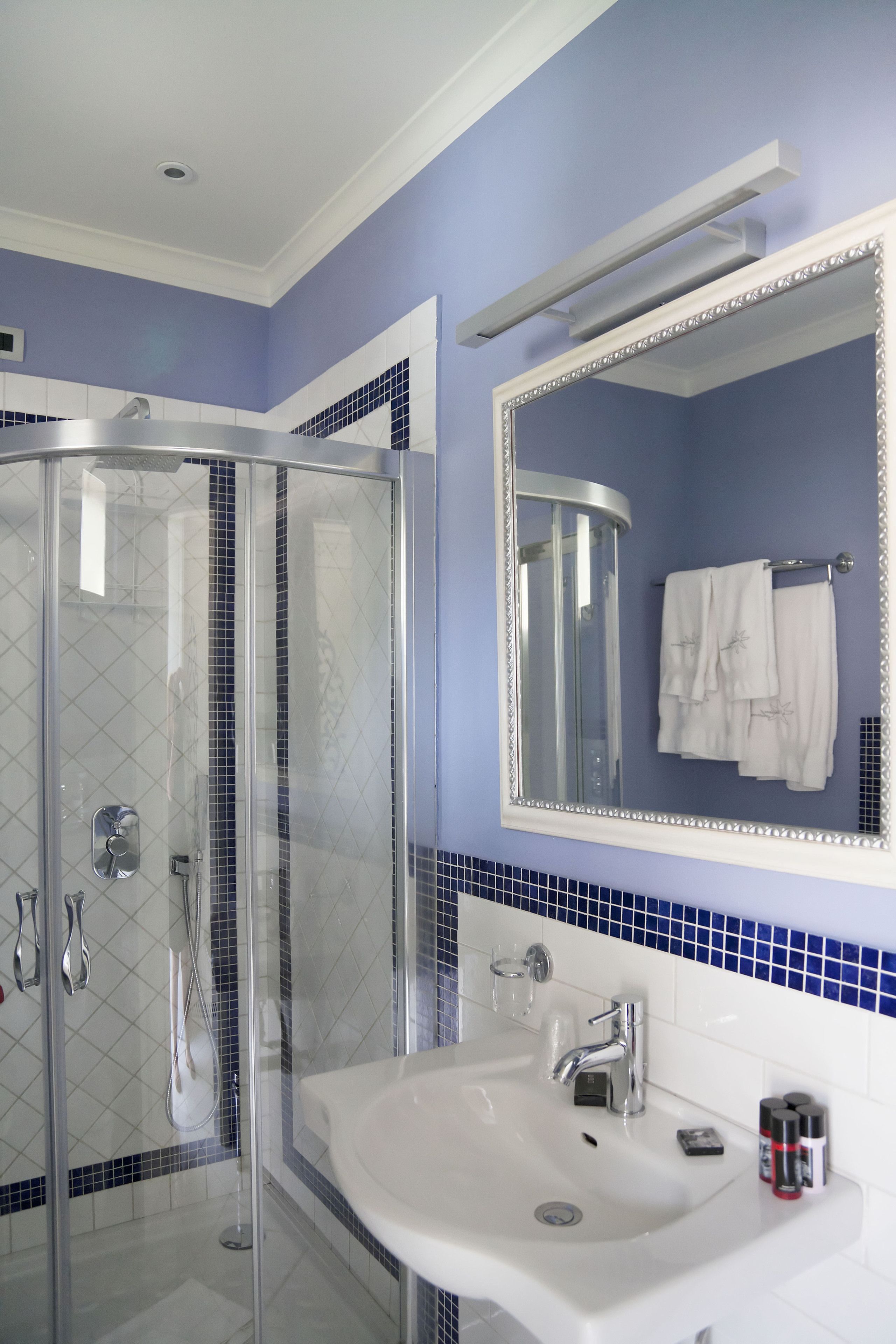 A bathroom with a glass-enclosed shower, a white sink, and a mirror with a decorative frame.