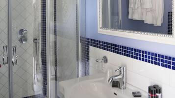A bathroom with a glass-enclosed shower, a white sink, and a mirror with a decorative frame.