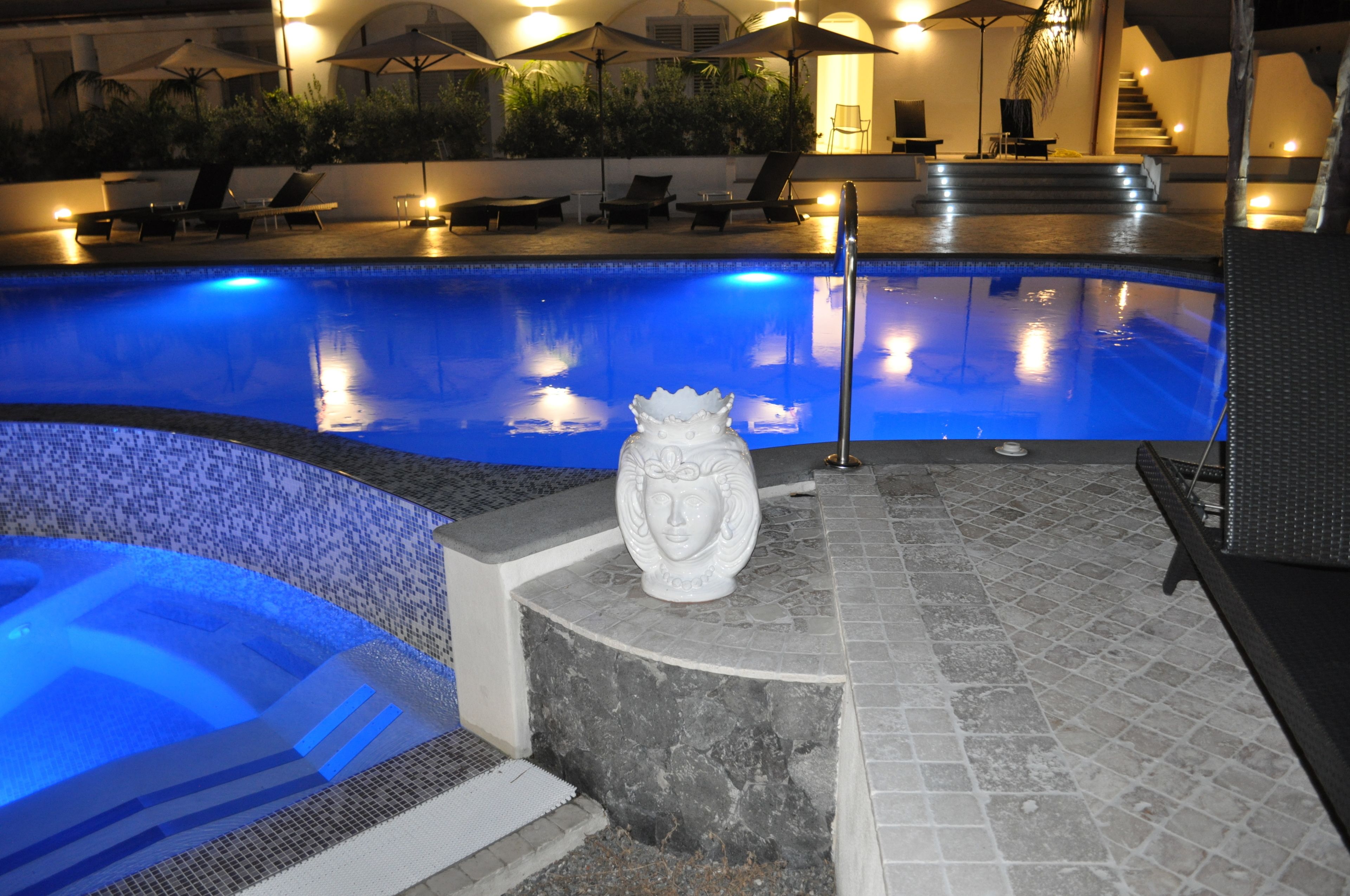 A swimming pool with a hot tub area, lounge chairs, and a decorative sculpture.