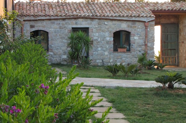 Un edificio de piedra con techo de tejas, un camino de piedra y diversas plantas.