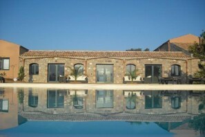 A stone building with a tiled roof, large windows, and a swimming pool in front.