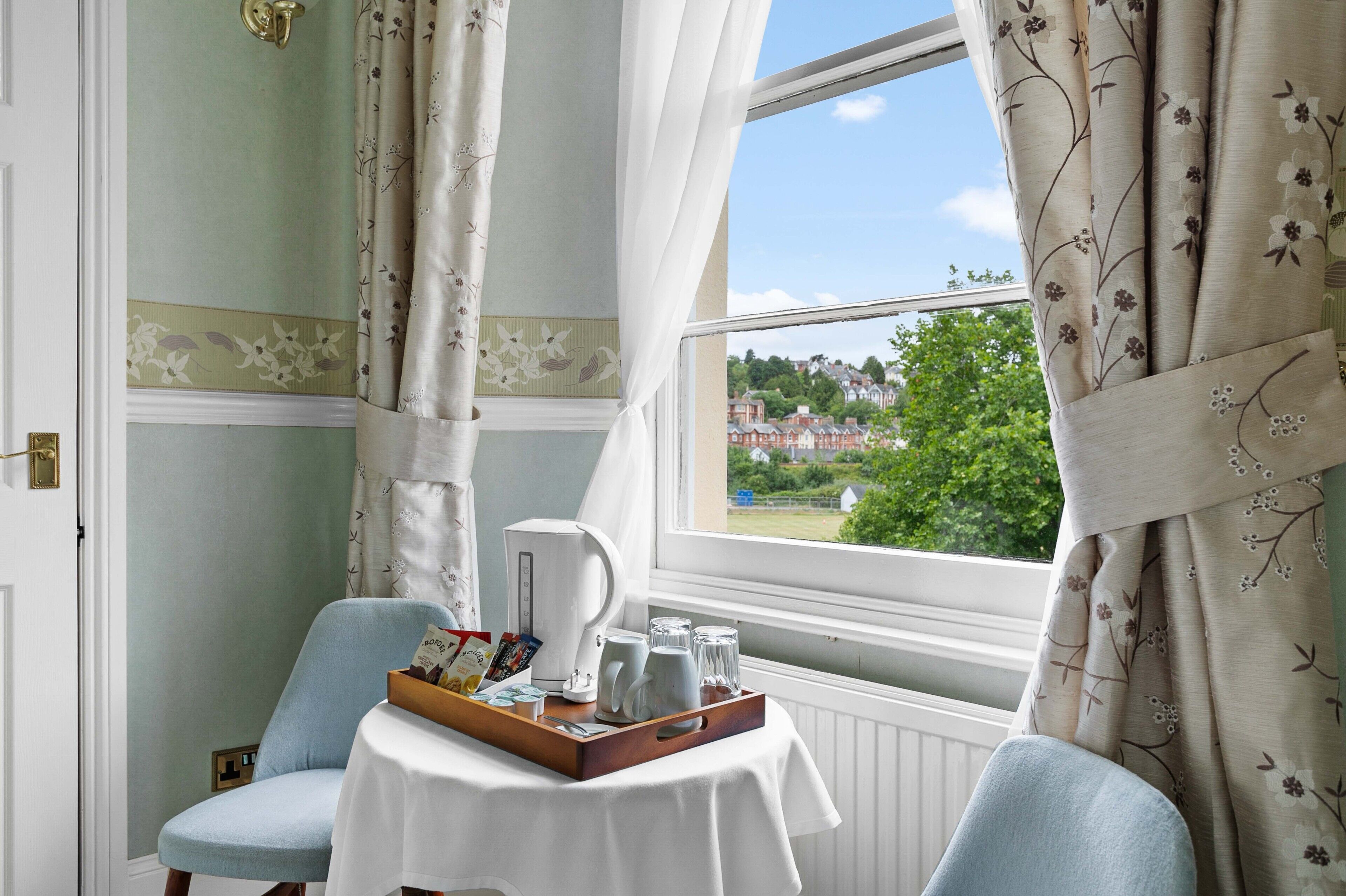 Ein Zimmer mit Blick auf eine grüne Landschaft, ein Tisch mit einer Servierttablett und ein Stuhl.