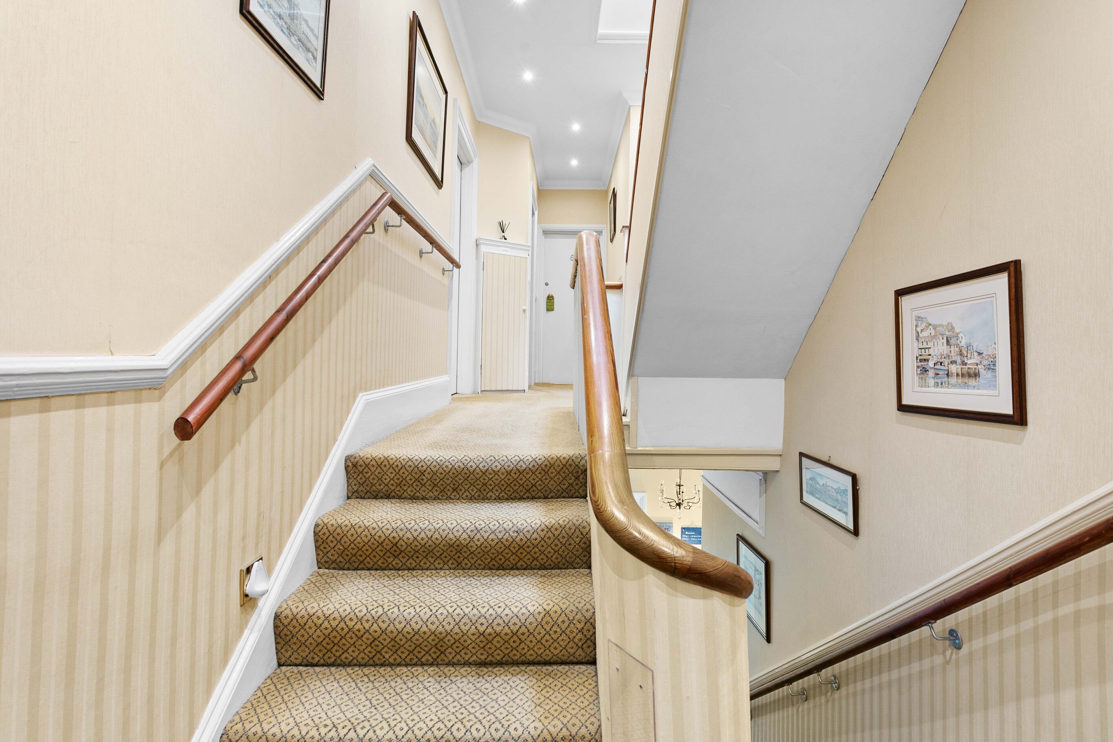 A staircase with patterned carpet, wooden handrails, and framed pictures on the walls.
