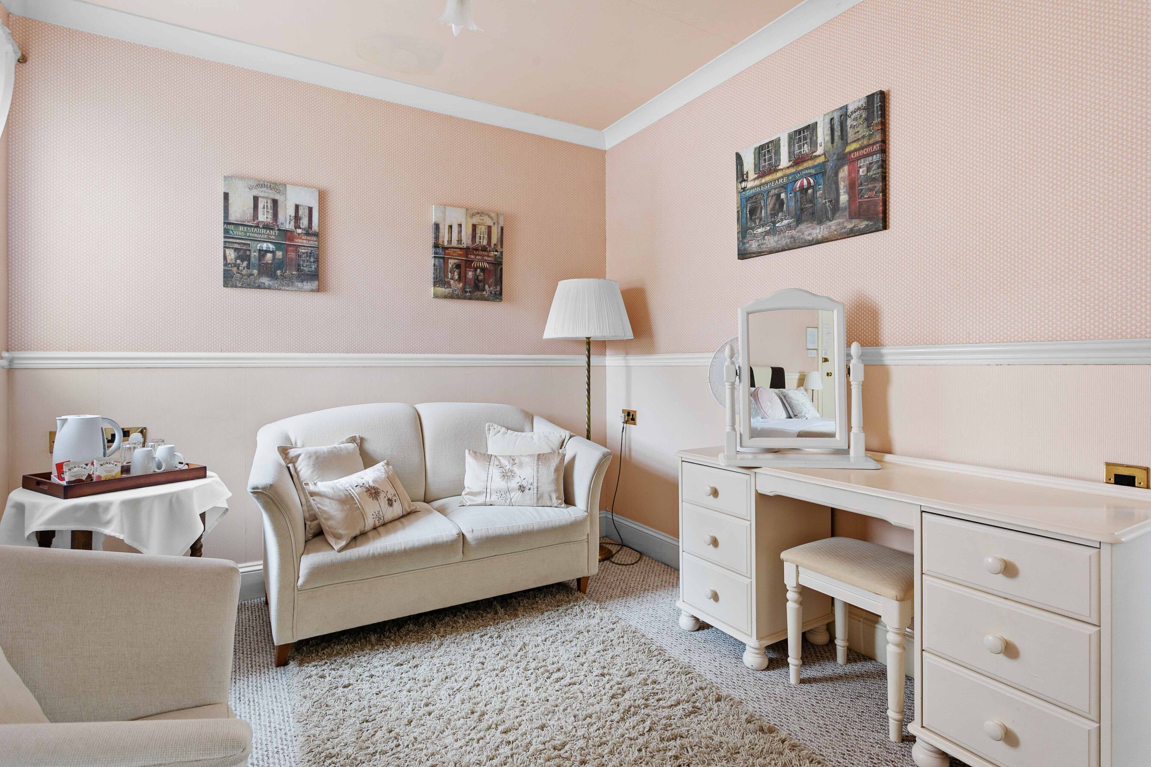 Une pièce avec un canapé blanc, un bureau avec des tiroirs, une lampe et deux tableaux accrochés au mur.