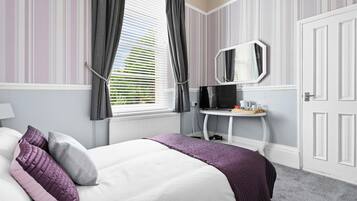 A bedroom with a bed, a bedside table with a mirror, a window with curtains, and a door.
